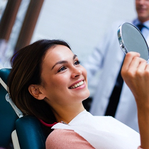 Woman with white teeth smiling in cosmetic dentist's mirror