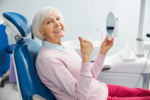 happy elderly woman looking into mirror in dental office 