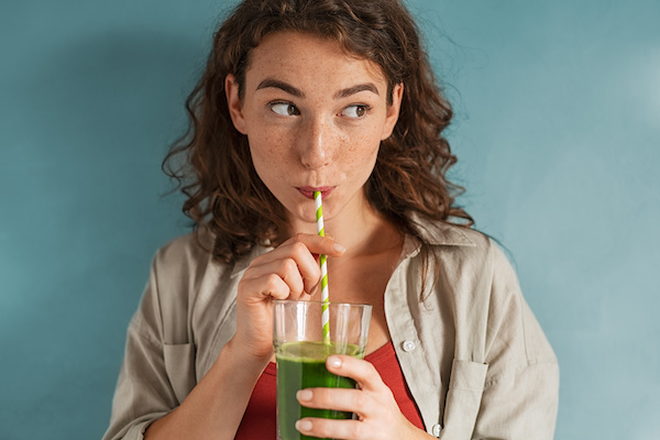 woman drinking green juice out of a straw