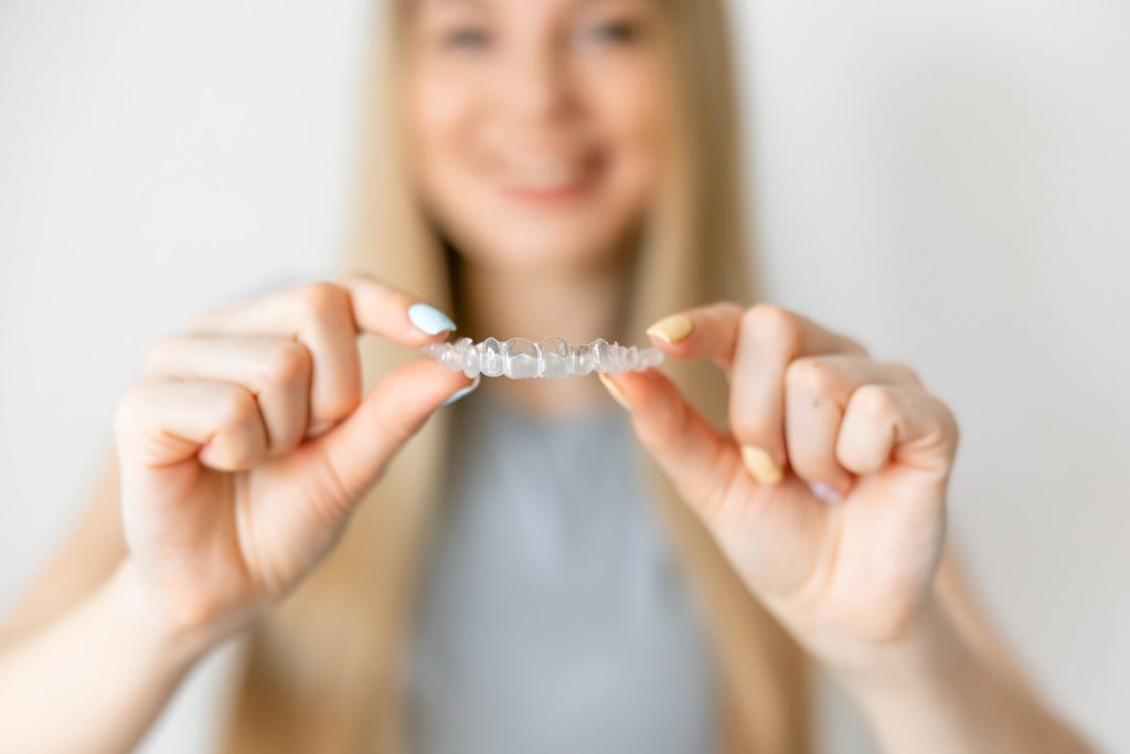 Smiling woman holding up Invisalign aligner